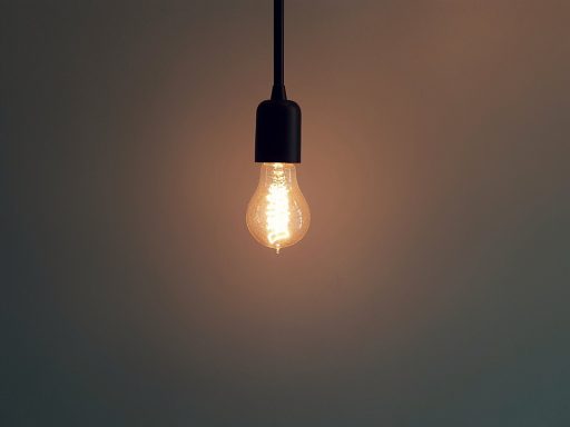 A dimly lit lightbulb hanging from the ceiling, shown against the bare wall of a room.