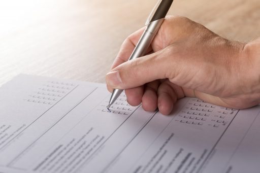 A man's hand filling in a paper survey with a pen.