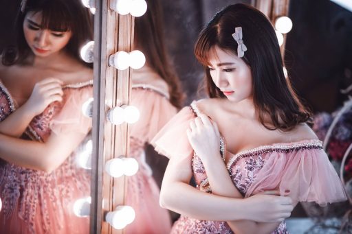 An image of an elegant Asian woman beside a mirror with lights surrounding it.