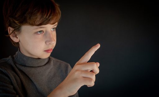 A boy holding his hand up in the air using his finger as a pointer.