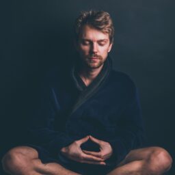 A man with his legs crossed and his eyes closed. He is deep in meditation. The man is wearing a blue gown.