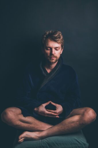 A man with his legs crossed and his eyes closed. He is deep in meditation. The man is wearing a blue gown.