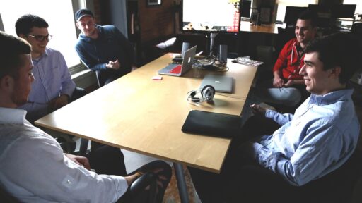 A team of software developers having an informal meeting around a table. There are laptops, headphones and other equipment on the table.